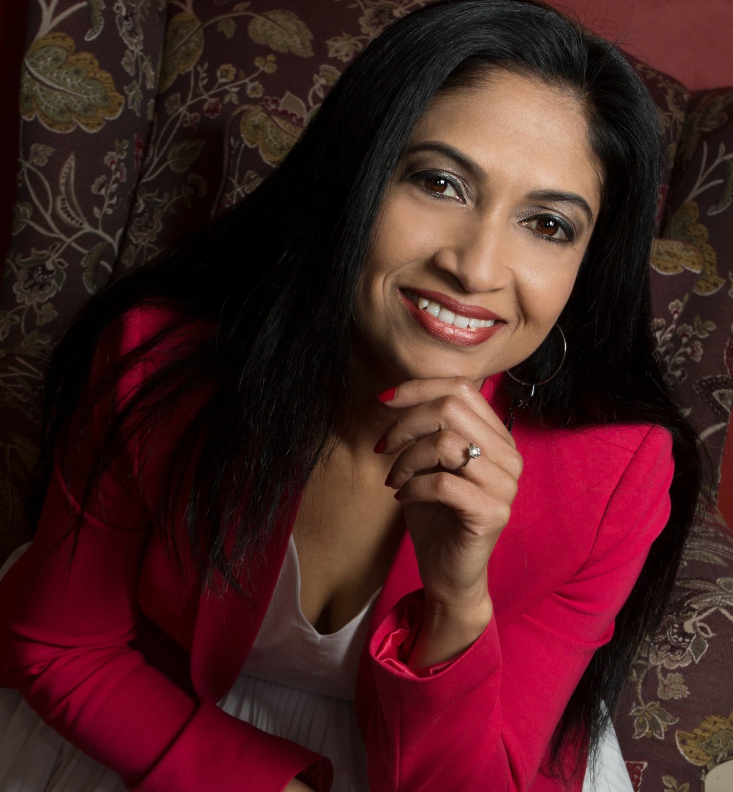 Reshmi Kumar, woman in a red jacket sitting on a patterned chair