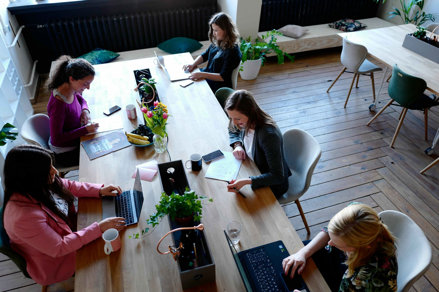 Group of people working together at a modern office desk with laptops and snacks.