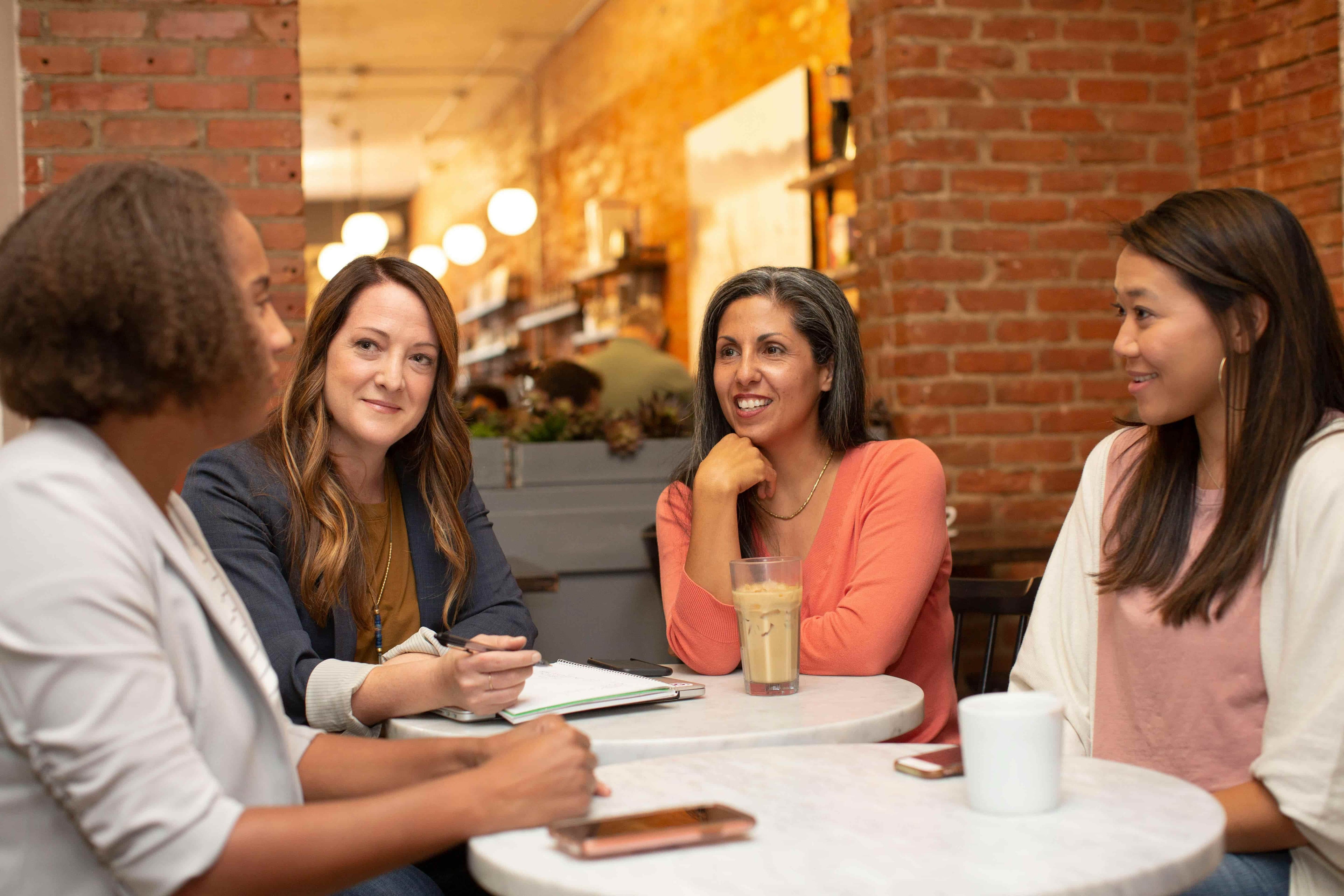 Four women sitting around a table in a casual setting, possibly a cafe or restaurant.